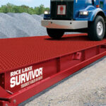 A red colored Rice Lake Survivor ATV Truck Scale sits below an 18 wheeler that's driving onto it..
