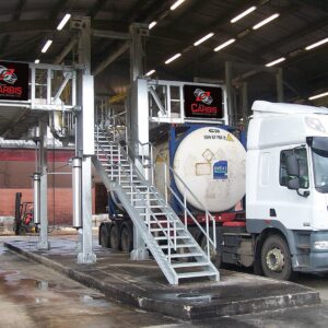 Two Carbis elevated truck platforms are separated by a ladder. A tank truck is parked underneath one of them.