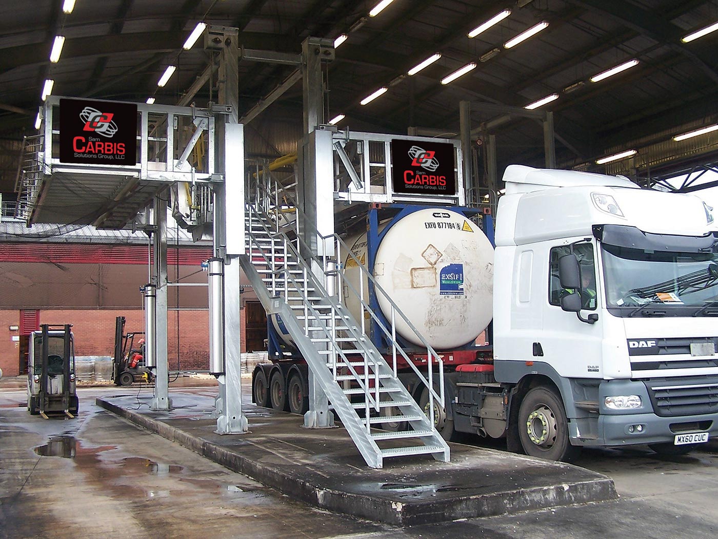 Two Carbis elevated truck platforms are separated by a ladder. A tank truck is parked underneath one of them.