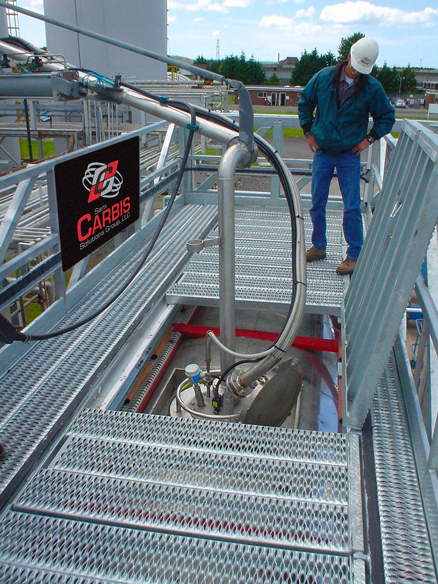 A man watches the hose apparatus pumping in fuel on top of a Carbis Solutions elevated tanker truck platform.