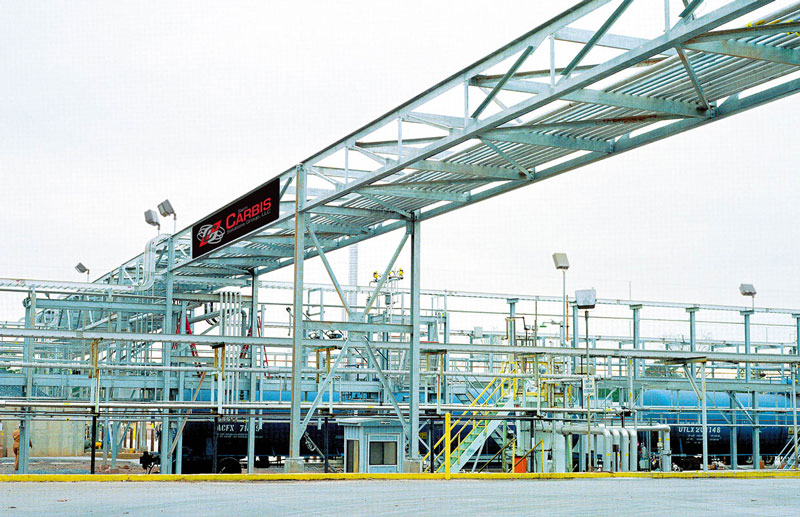 A Carbis solutions pipe rack extends over an asphalt area where trucks can come load fuel.