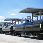 Multi-hatch loading bays tower over tanker railcars on a track.