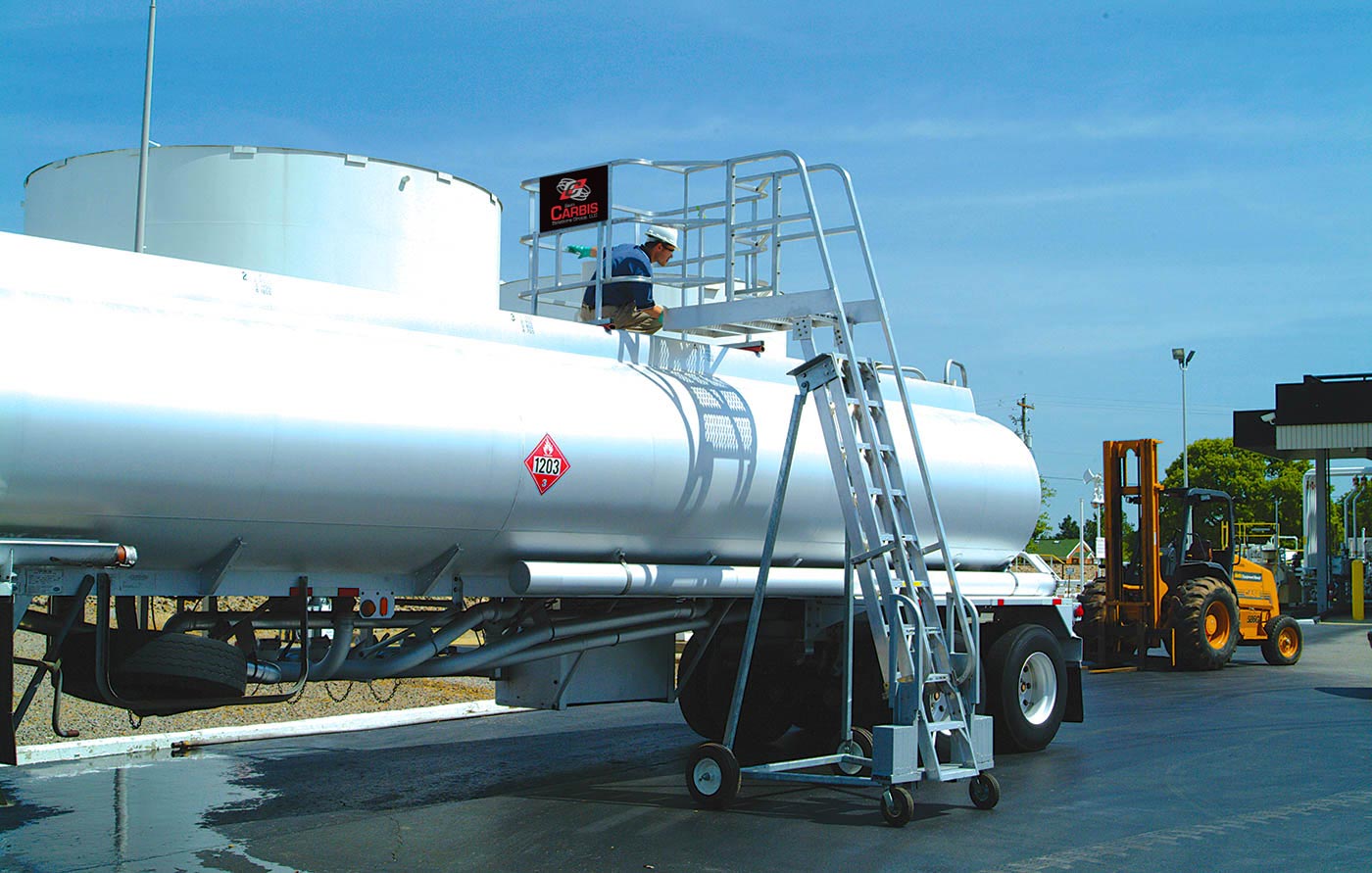 A Carbis portable tanker truck access system is pulled up onto a tank car with a man on the unit.