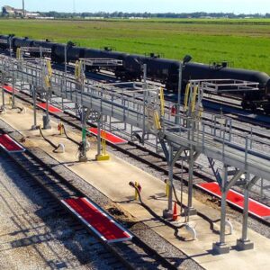 A catwalk runs down a group of railcar unit train enclosures in the middle of two rail tracks.