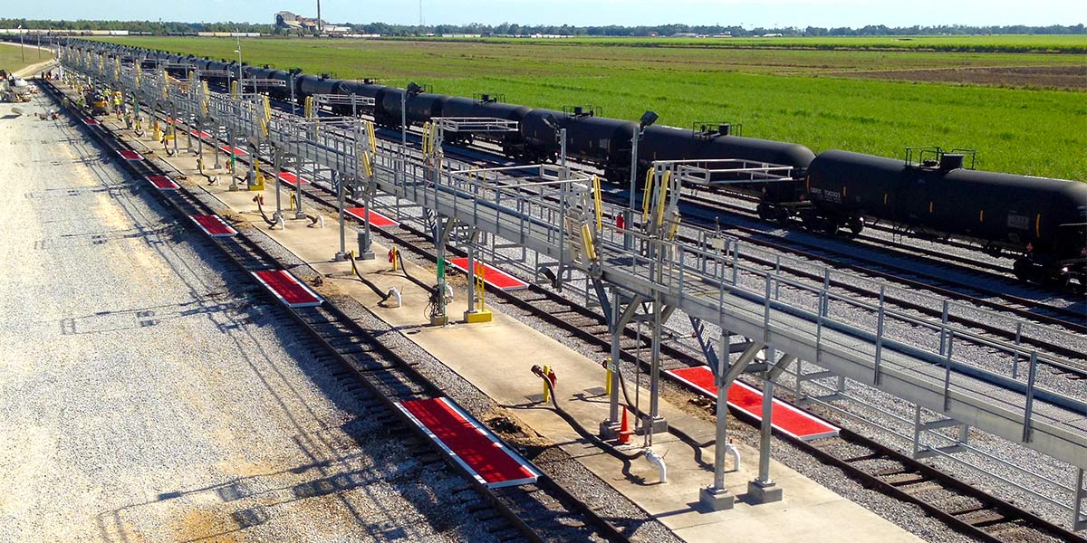 A catwalk runs down a group of railcar unit train enclosures in the middle of two rail tracks.