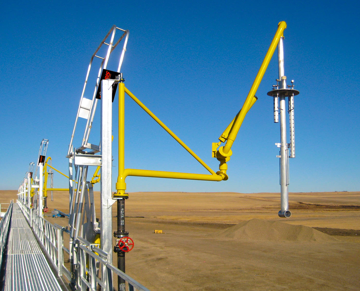 A top loading arm sits above a catwalk on a loading platform.