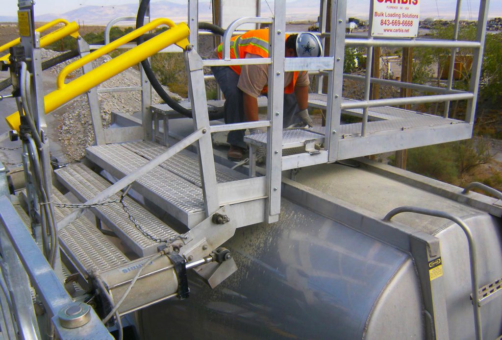 A worker is on a gangway in a custom safety cage, standing on a tanker truck.