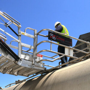 A worker stands on a Carbis Solutions folding stairs gangway enclosure above a tanker car.