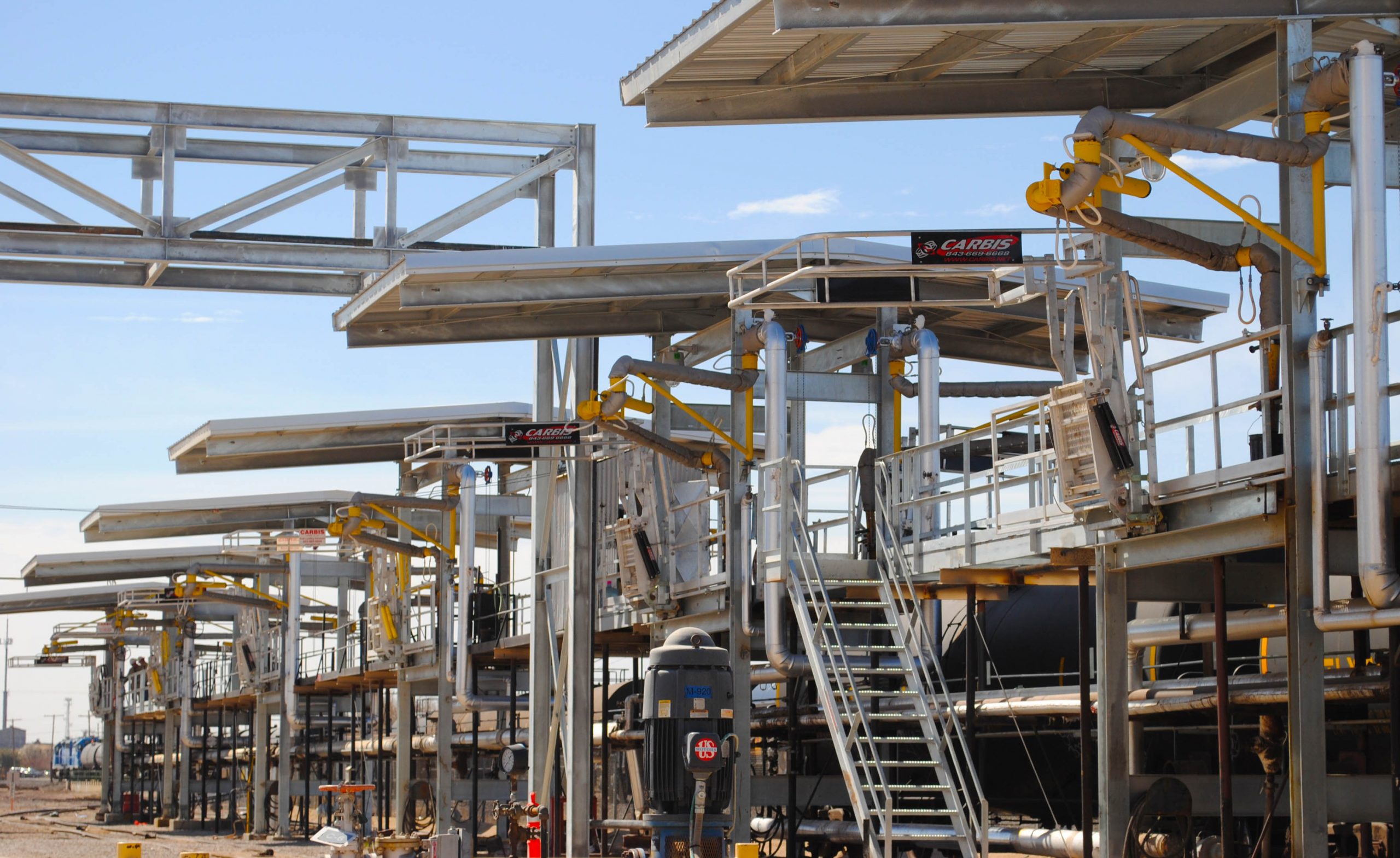 A loading dock is shown with multiple docking bays and top loading arms and safety cages in each bay.