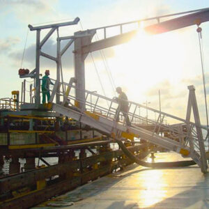 Workers traverse a marine gangway on a barge.