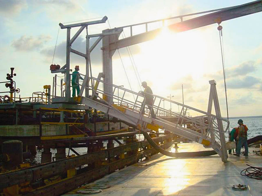 Workers traverse a marine gangway on a barge.