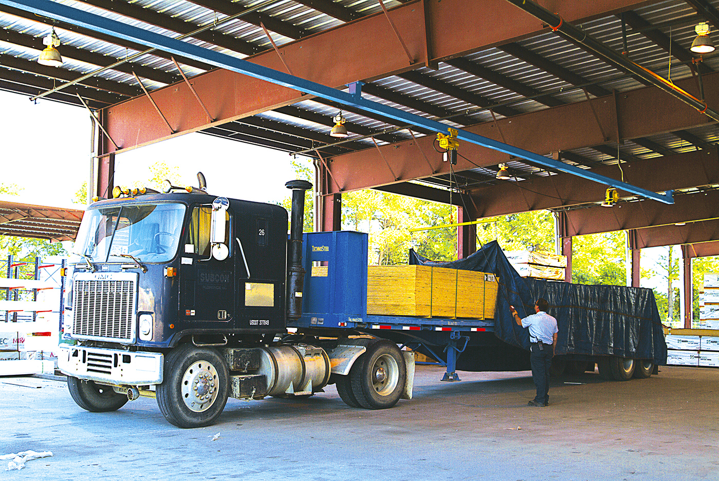 A truck's load is being tarped with an overhead tarping solution.