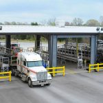 A flatbed tarping dock with several stalls and a loaded 18 wheeler being tarped.