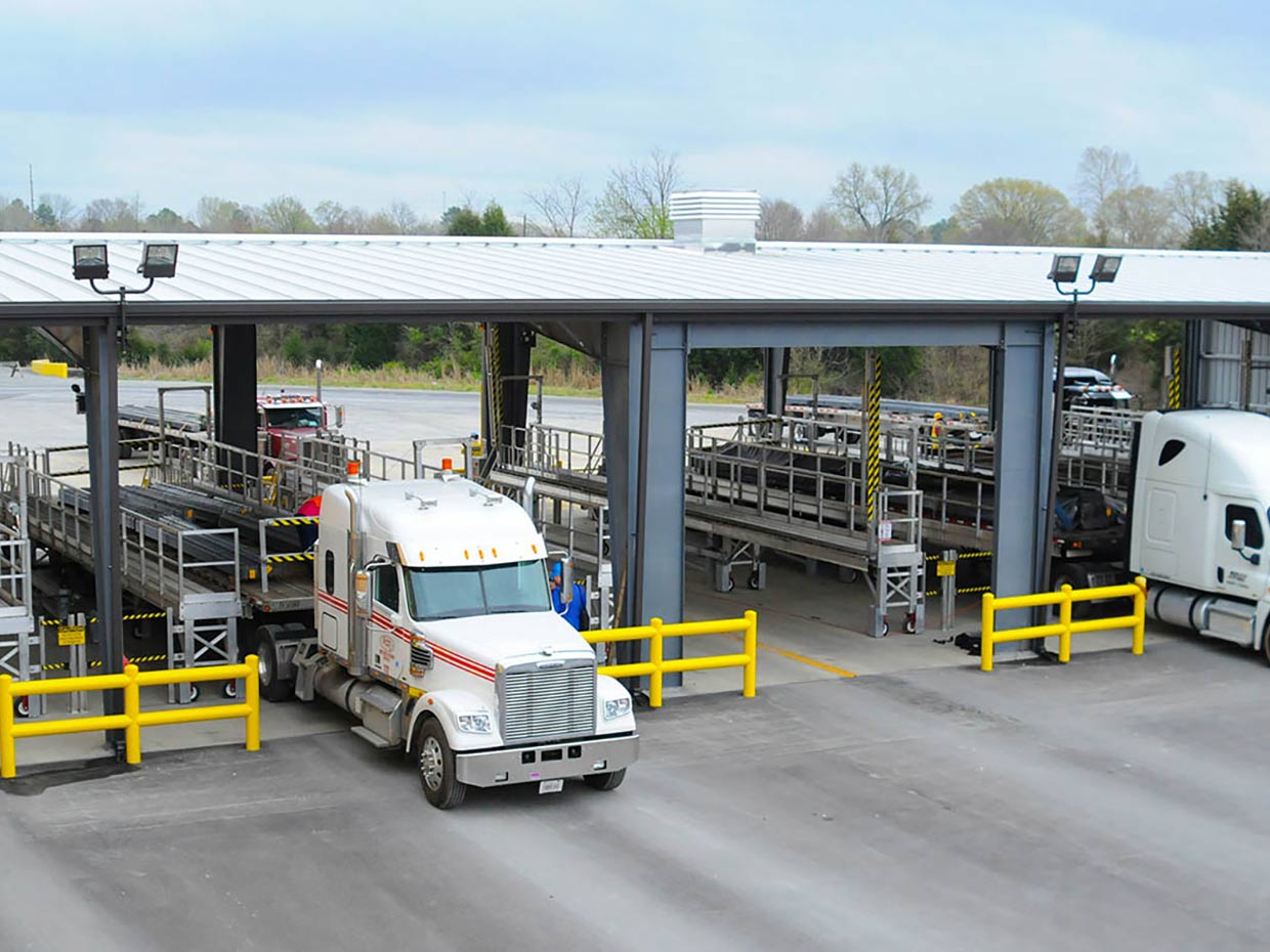 A flatbed tarping dock with several stalls and a loaded 18 wheeler being tarped.