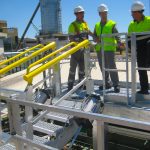 Workers stand on a Carbis Solutions folding stairs gangway enclosure above a tanker car.